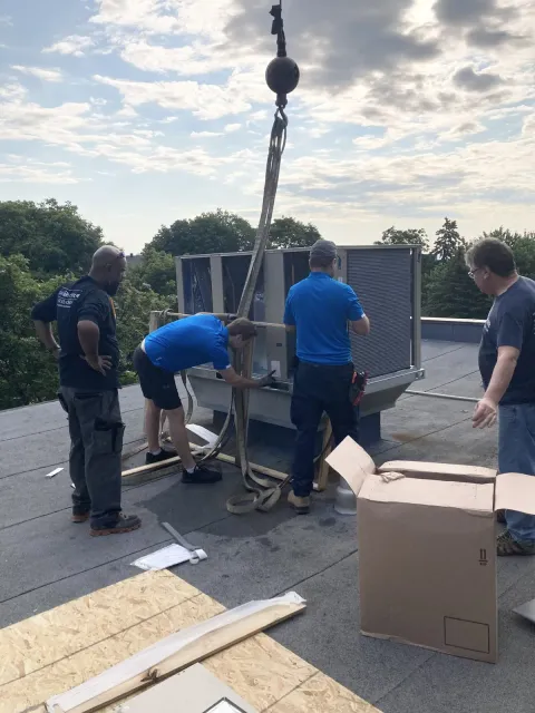 A JCD crew guiding a replacement rooftop unit lifted by crane