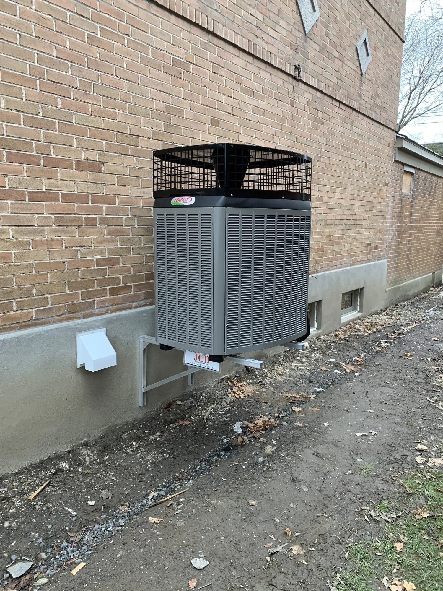 Une unité extérieure de thermopompe Lennox sur un support mural, contre une maison en brique