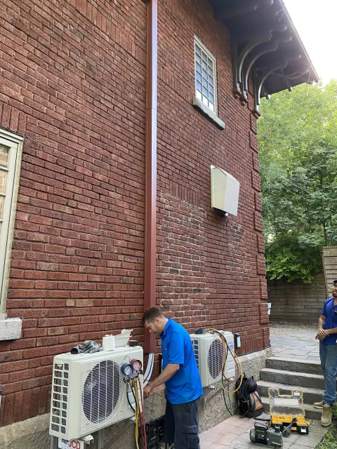 A JCD technician with gauges connected to two ductless heat pump outdoor units